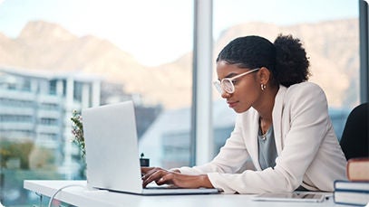 A person sitting at a desk by a window while working on a laptop.