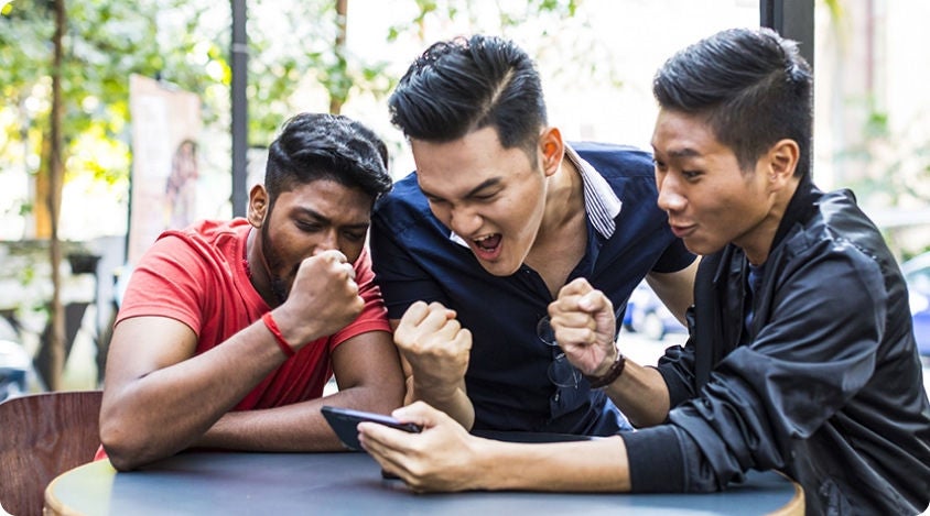 Group of three men cheering and smiling while reacting to something on a smartphone.