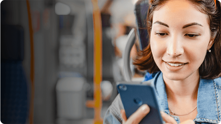A person holding a smartphone while seated on public transportation, with yellow poles and seats visible in the background.