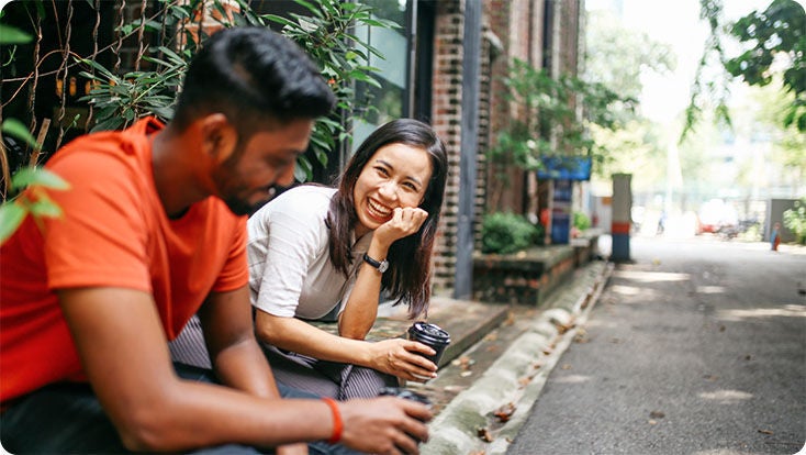 Two people having coffee sitting on a curb outdoors.