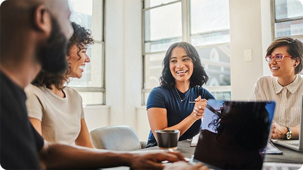 Four people sitting at a desk  in a meeting room smiling.