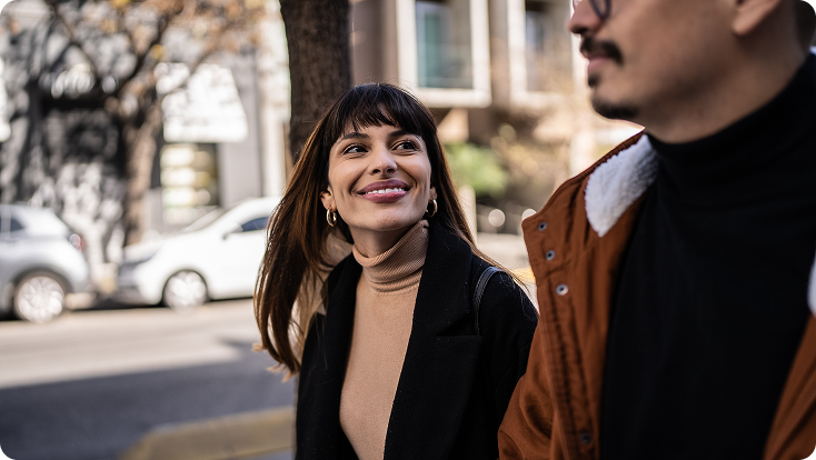 Smiling woman and man walking together outdoors, carrying shopping bags in a shopping district.