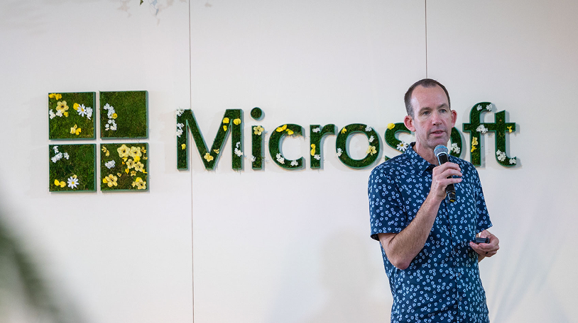 Tim Frank presenting in front of a Microsoft logo made of moss and flowers.
