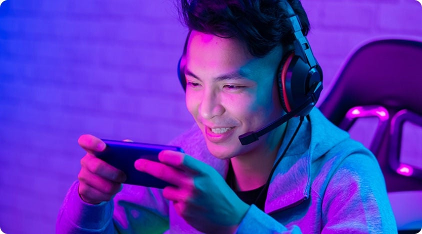 Person wearing a headset and smiling while playing a mobile game in a room lit with bright neon colors.