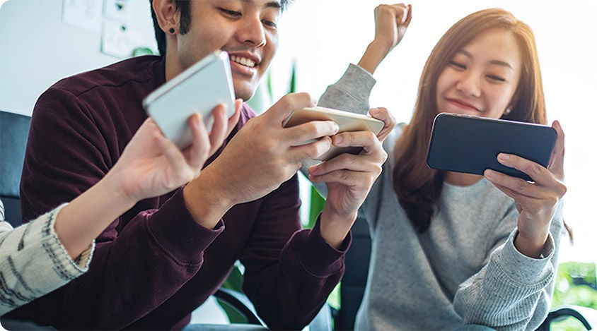 Three people smiling and playing mobile games together, each holding a phone 