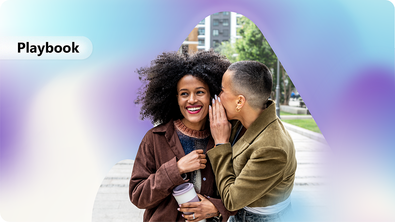 The image shows a close-up of two people, one with curly hair and one with straight hair, holding hands and smiling, standing on a sidewalk with a city backdrop.
