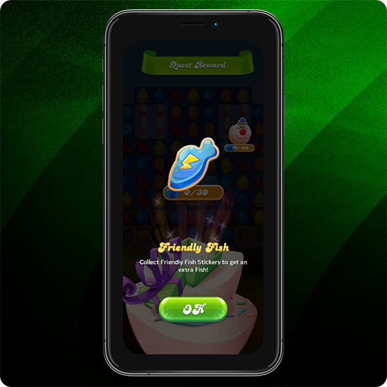 Smartphone displaying a candy-themed game reward screen with a blue fish-shaped icon labeled “Friendly Fish,” text explaining to collect stickers for an extra fish, and a green “OK” button, set against a green striped background.