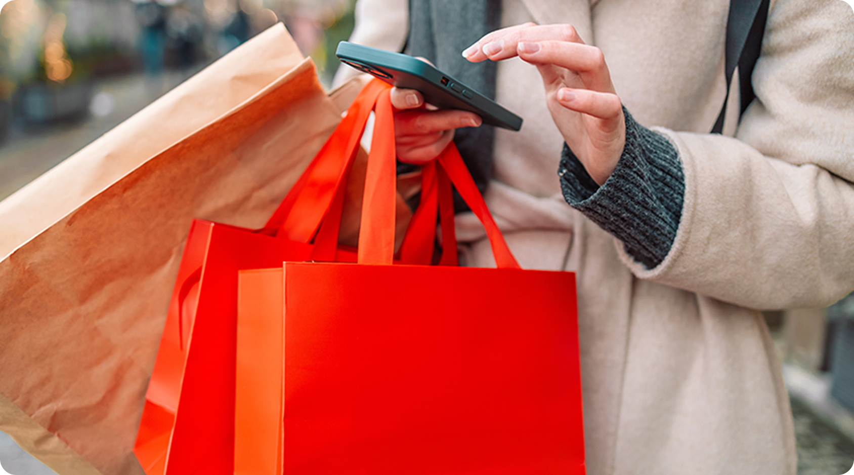 Person carrying red shopping bags and using a smartphone while out shopping.