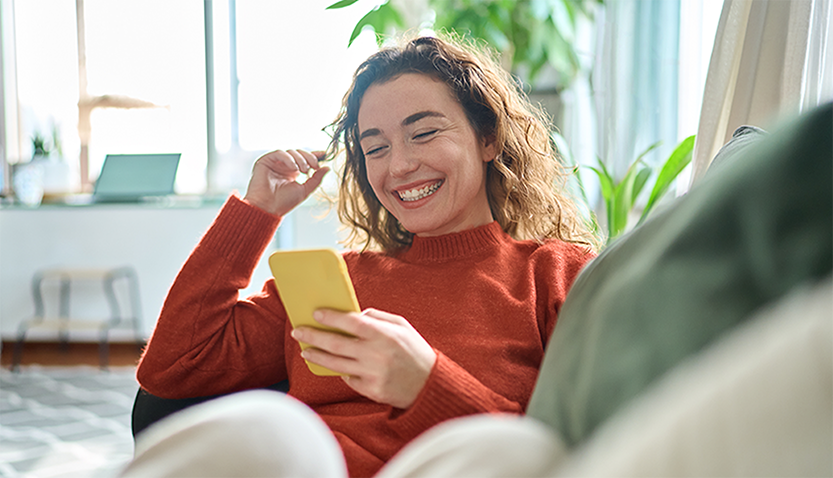 Woman smiling while looking at her smartphone, seated comfortably at home 