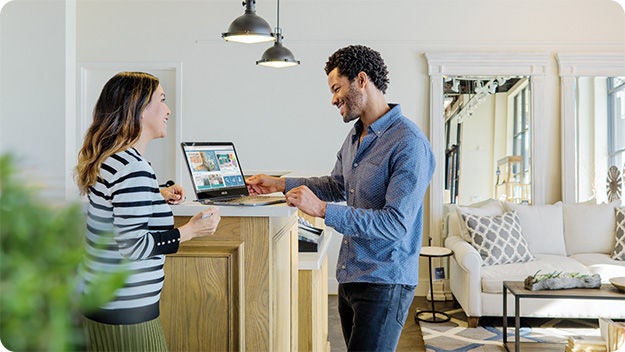 Two people standing indoors by a counter using a laptop.