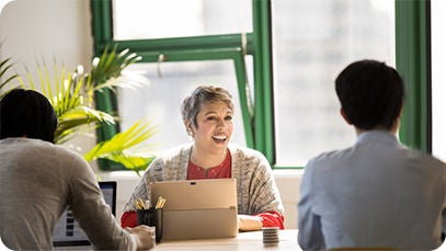 Trois personnes assises à une table, une personne sourit tout en utilisant une tablette.