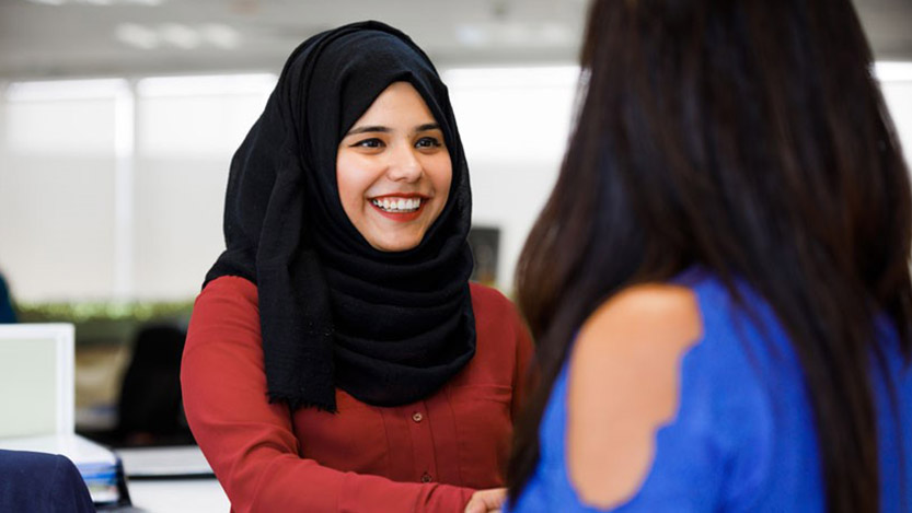 A woman smiles and looks directly at another woman that has her back to the camera.