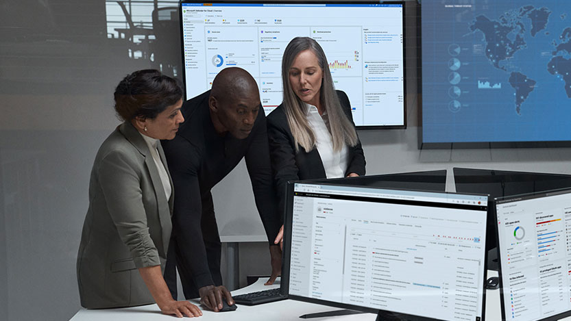 Three people surrounded by monitors analyze something on one of the screens.