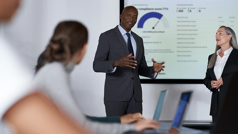 Two people stand in an office while giving a presentation.