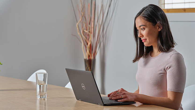 A woman sitting at a table works on her laptop computer.