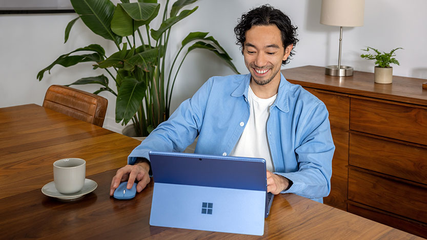 A man sitting at a table smiles while working on his laptop computer.