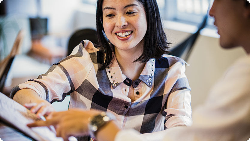 Two coworkers talking and smiling while using a laptop at an office.