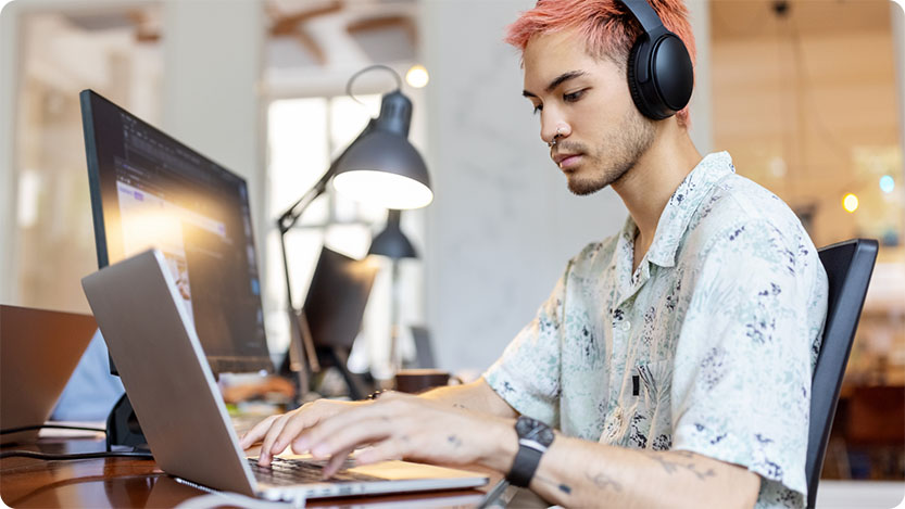 Person with headphones sitting at a desk, working on a laptop.