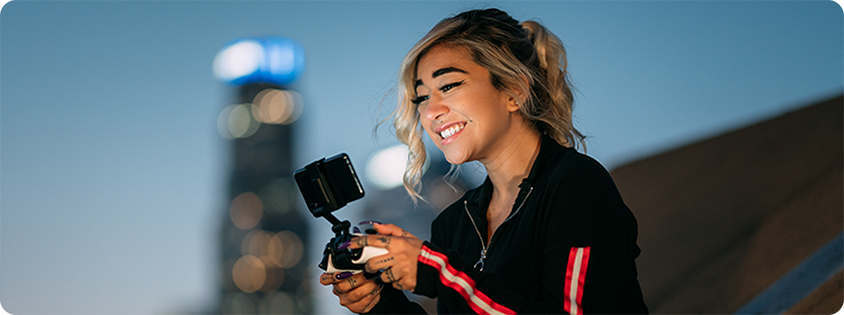 Person sitting outdoors at dusk, smiling while using a controller with a phone mounted on top to play a mobile game