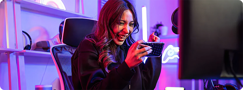 Woman sitting at a gaming desk, celebrating while playing a mobile game in a room with colorful LED lighting
