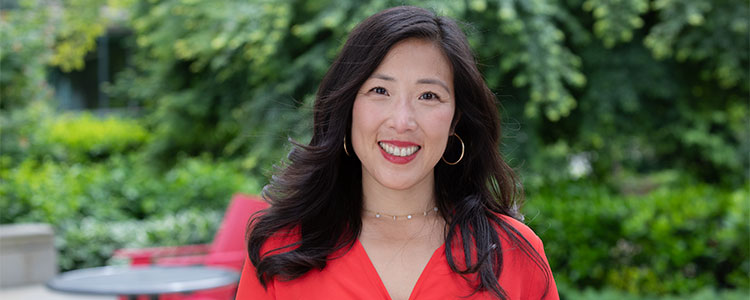 A woman out in a garden smiles directly at the camera.