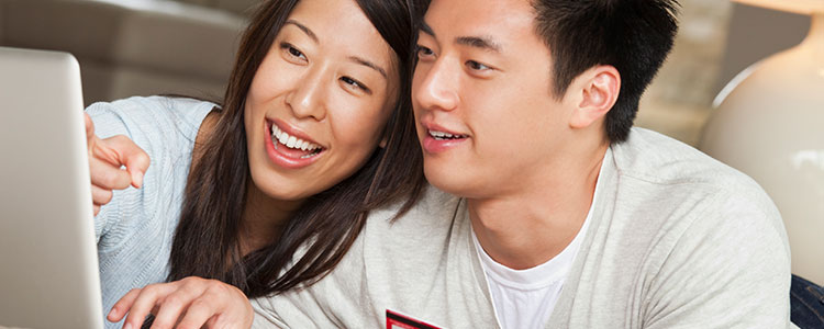 Two people smile while working on a laptop.